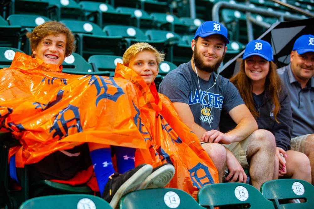 A group of tiger's fans wearing the gsvu night hats are sitting in their seats for the game, smiling for the camera. the two teenagers are covered in ponchos